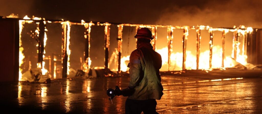 Firefighter silhouetted against a burning building after a house fire, illustrating a home insurance claim.