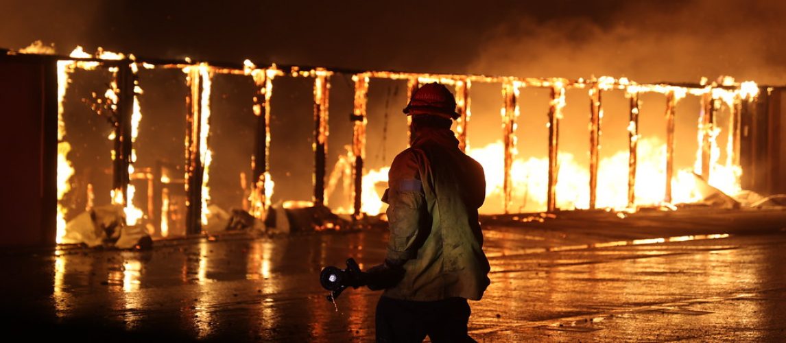 Firefighter silhouetted against a burning building after a house fire, illustrating a home insurance claim.